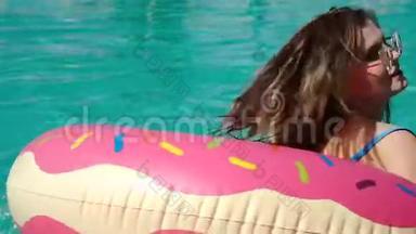 阳光明媚的夏日，一位年轻貌美的<strong>女士</strong>戴着黑色<strong>比基尼</strong>的太阳镜，躺在充气的粉红色甜甜圈里漂浮在游泳池里